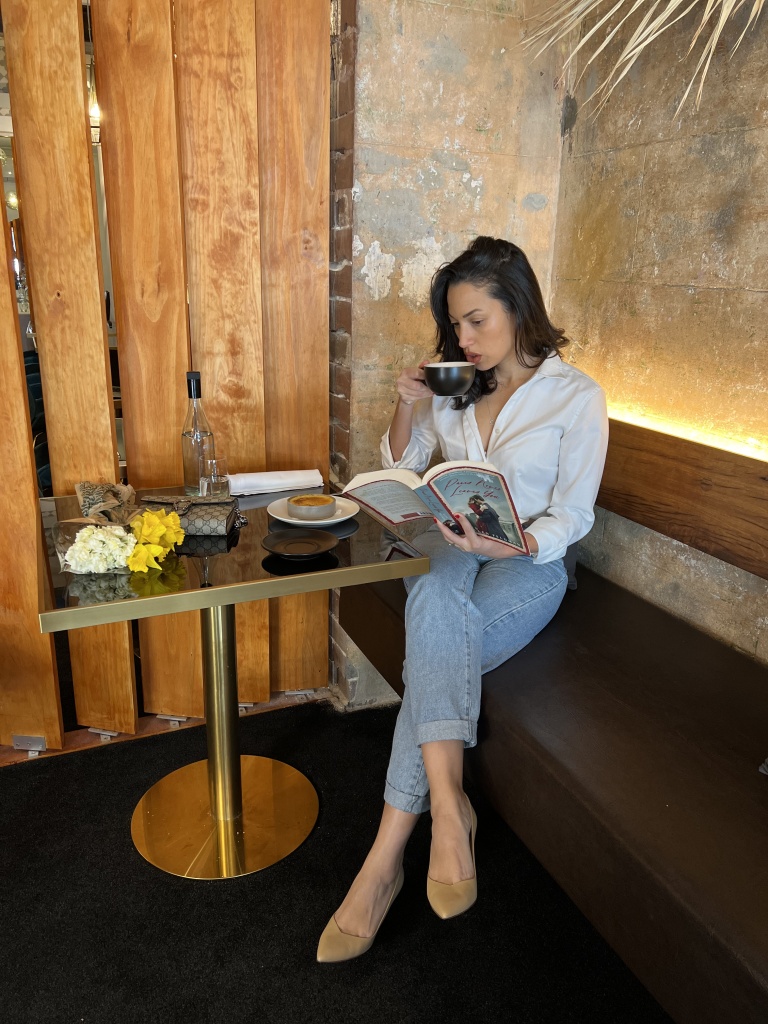 model in a cafe reading a book wearing a white button down shirt, blue jeans and Sarah Flint perfect pump stiletto heels with a Gucci wallet on chain on the table